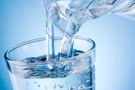 Un bicchiere trasparente viene riempito con acqua fresca e limpida, creando bollicine sulla superficie.