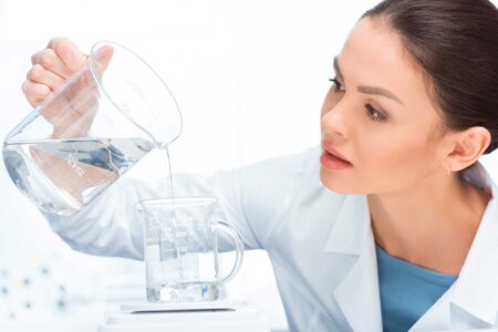 Una scienziata in camice bianco versa del liquido trasparente da un becher a un altro becher in un laboratorio.
